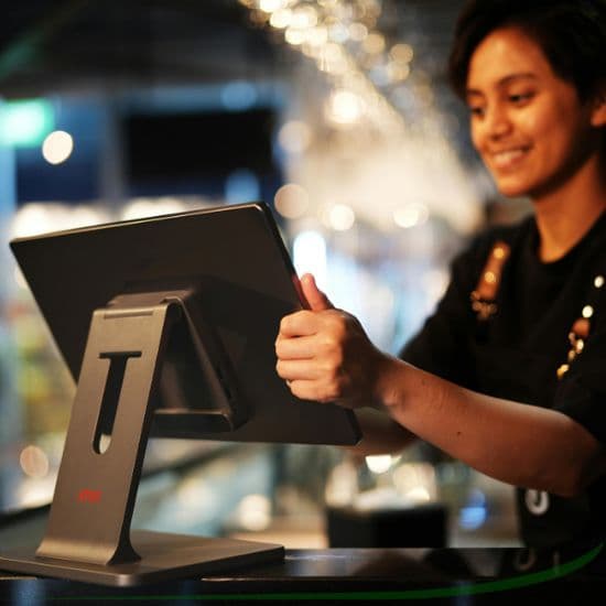 Smiling cashier using a touchscreen POS terminal at the counter